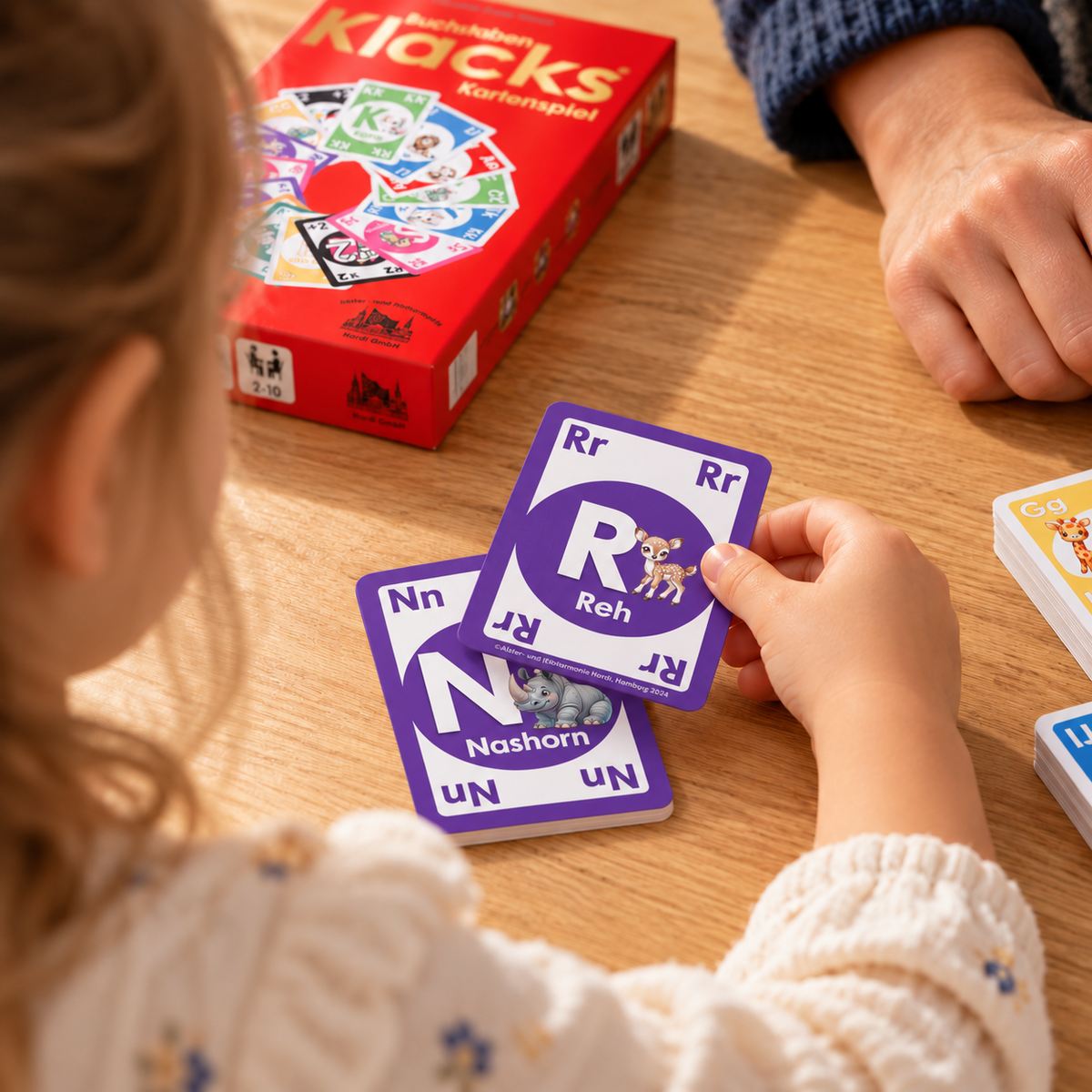 Kind legt die lila Karte R wie Reh auf die lila Karte N wie Nashorn – bei Buchstaben Klacks hilft die Farbe beim Mitspielen